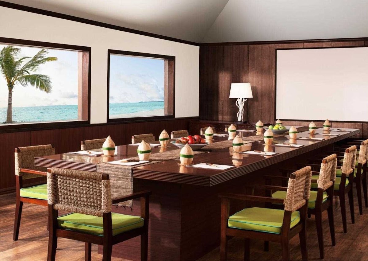 Conference room with woven chairs, long wooden table, and ocean views through large windows at Taj Exotica Resort & Spa Maldives.