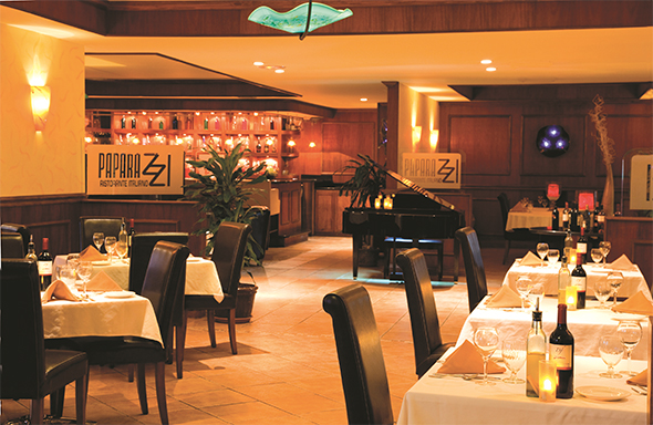 Papaya's restaurant dining room with white tablecloths, black chairs, a grand piano, and warm amber lighting at Tamarijn Aruba.