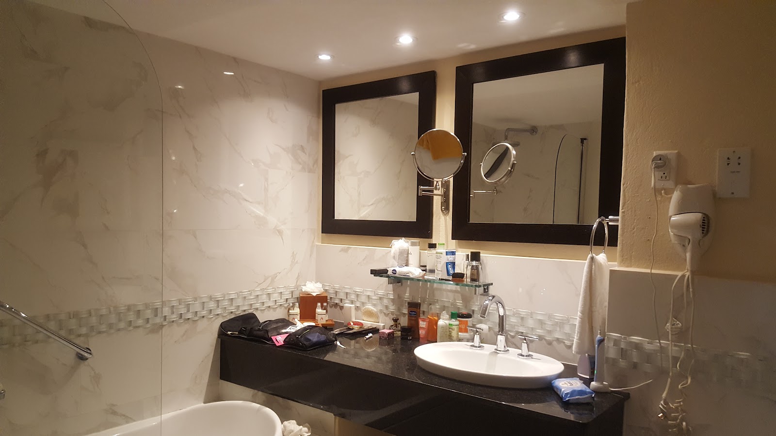 Bathroom at Tamarind Barbados with dual sinks, black vanity, framed mirrors, marble shower enclosure, and toiletries on counter.