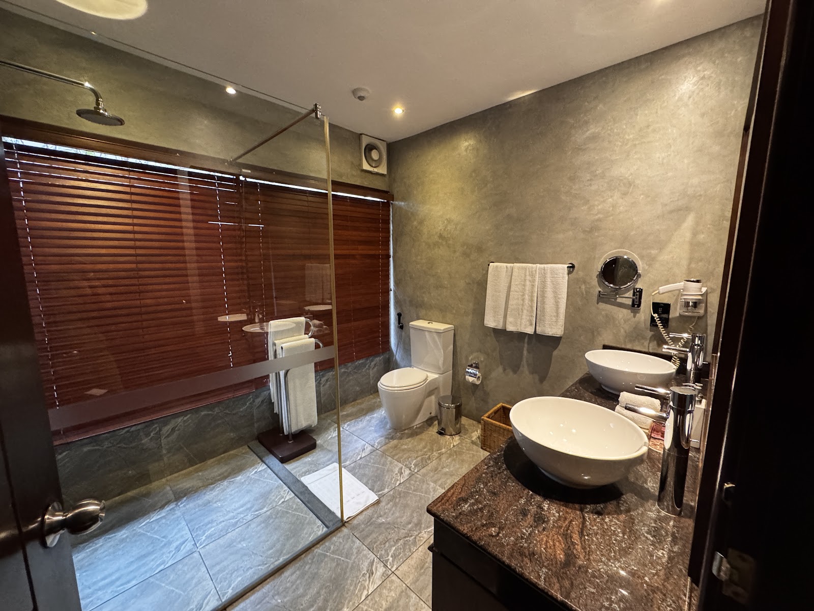 Spacious bathroom with dual white vessel sinks, walk-in shower with glass enclosure, and gray textured walls at The Bay an Uga Experience.