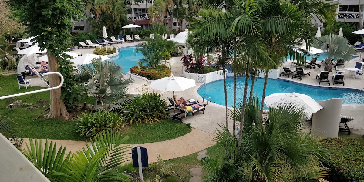 The Club Barbados Resort & Spa pools surrounded by palm trees, lounge chairs, and whitewashed cabanas.