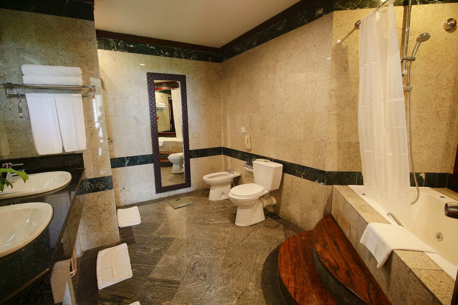Spacious bathroom at The Eden Beruwala with dual sinks, separate toilet, soaking tub, and walk-in shower with travertine and dark tile accents.