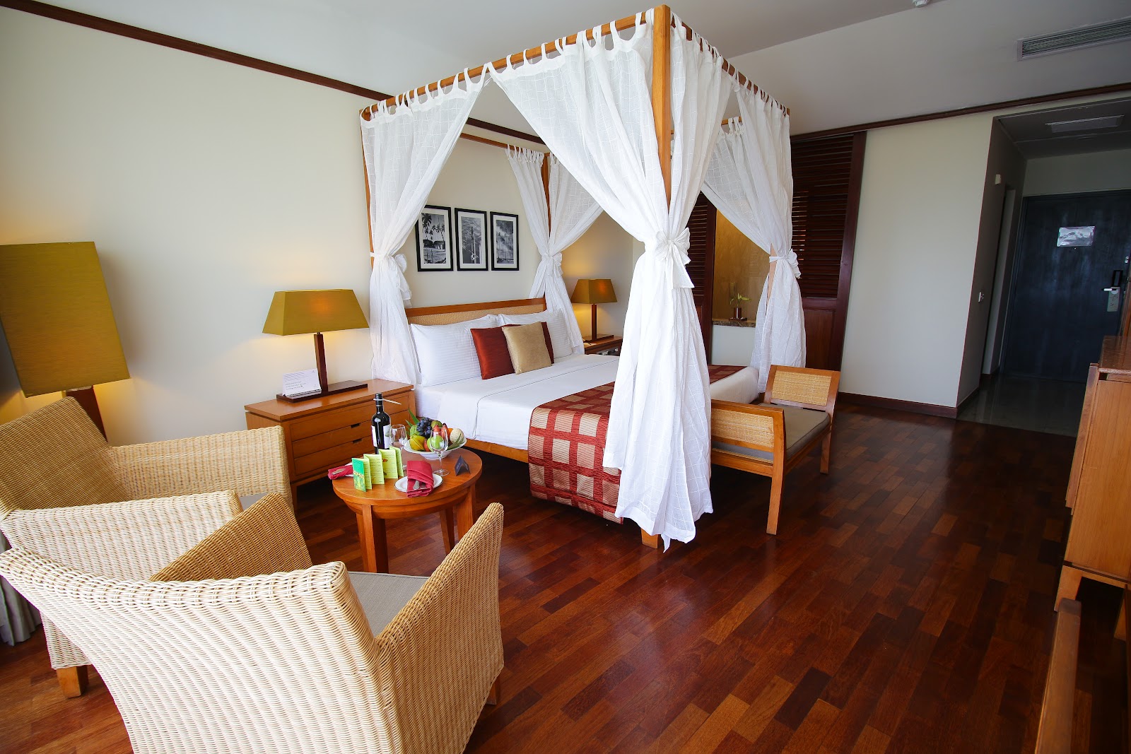 Modern bedroom at The Eden Beruwala with dark wood flooring, queen bed, and floor-to-ceiling windows overlooking tropical landscape and ocean.