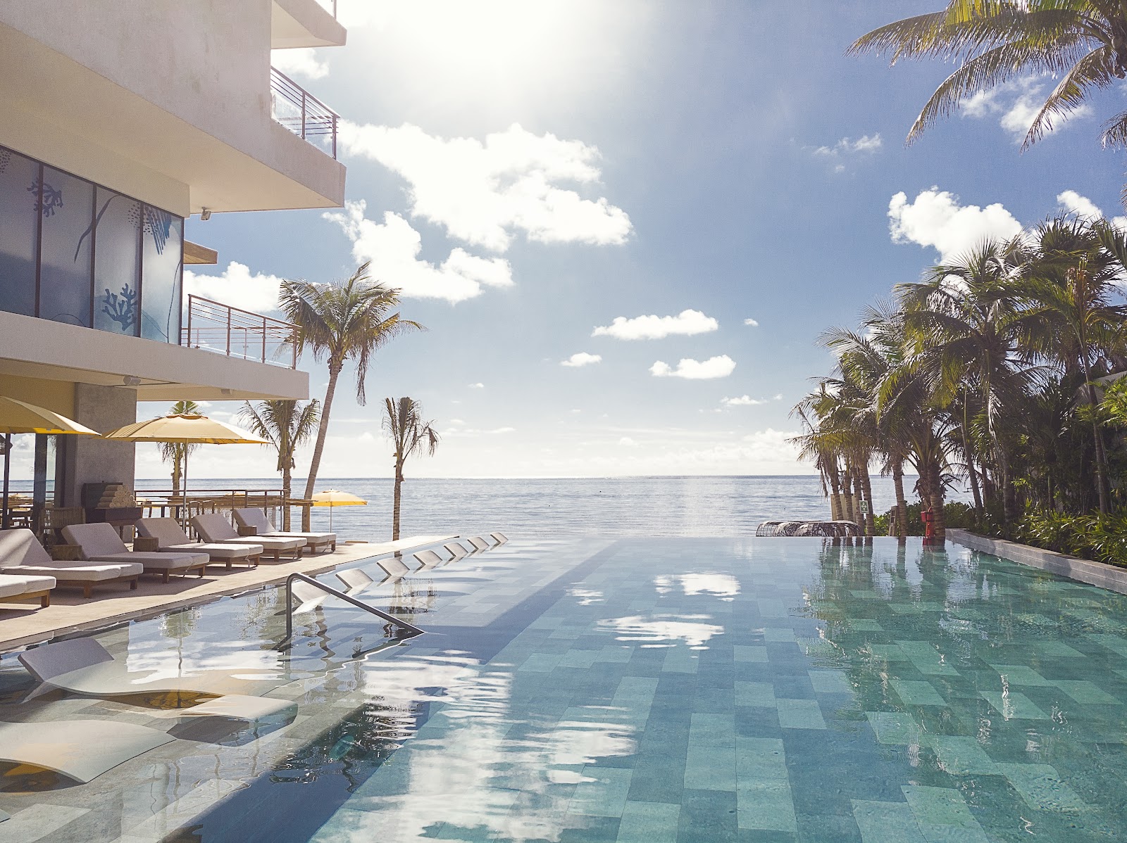 Infinity pool overlooking the ocean at The Fives Oceanfront Riviera Maya, with loungers, palm trees, and modern beachfront architecture.