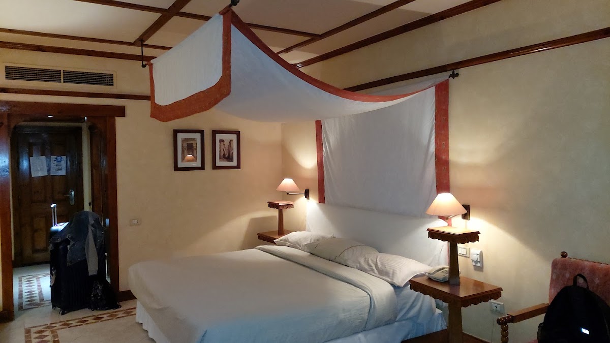 Four-poster bed with red and white draped canopy in a guest room with dark wood beams and bedside lamps.
