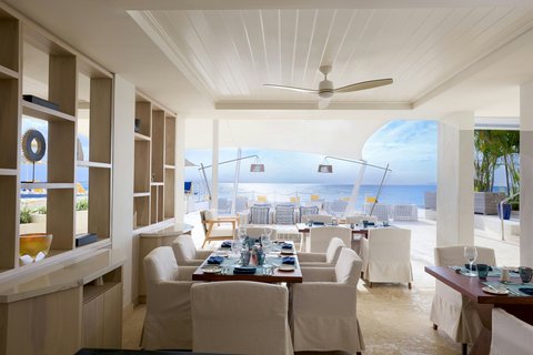 The House Barbados suite features cream furnishings, built-in shelving, and expansive windows overlooking the Caribbean Sea and coastline.