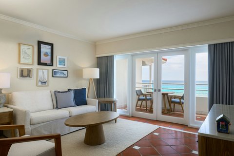 Oceanview suite at The House, Barbados with cream sofa, framed art, and glass doors opening to a terrace overlooking turquoise water.