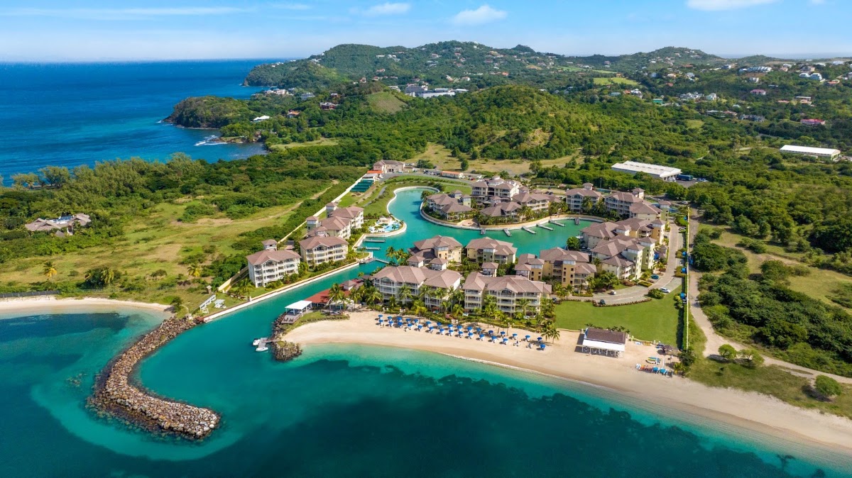 Aerial view of The Landings Resort and Spa on a forested St. Lucia hillside with turquoise lagoon, sandy beach, and Caribbean Sea beyond.