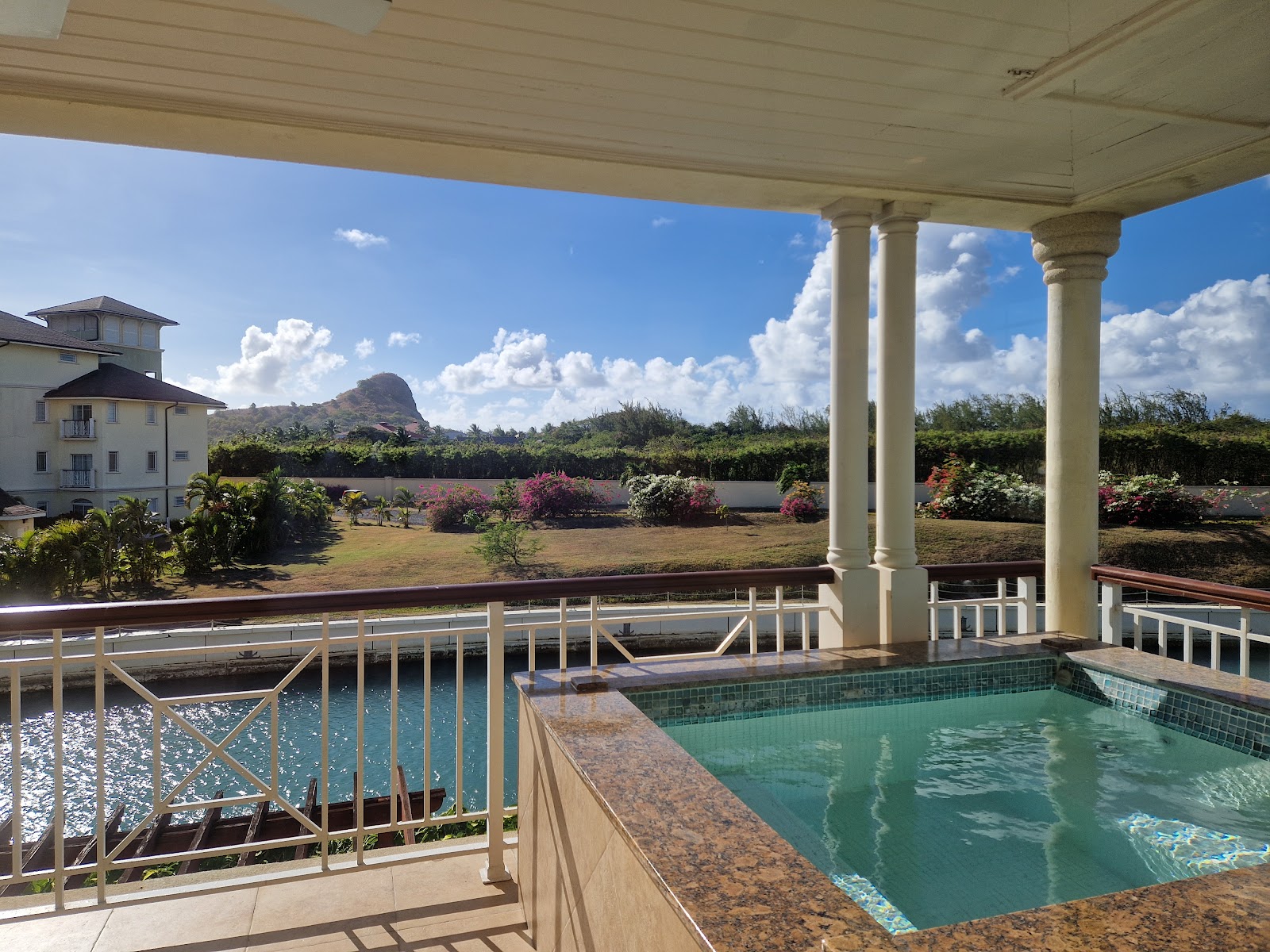 Covered poolside terrace at The Landings Resort and Spa with turquoise pool, mountain view, and flowering gardens beyond white railings.