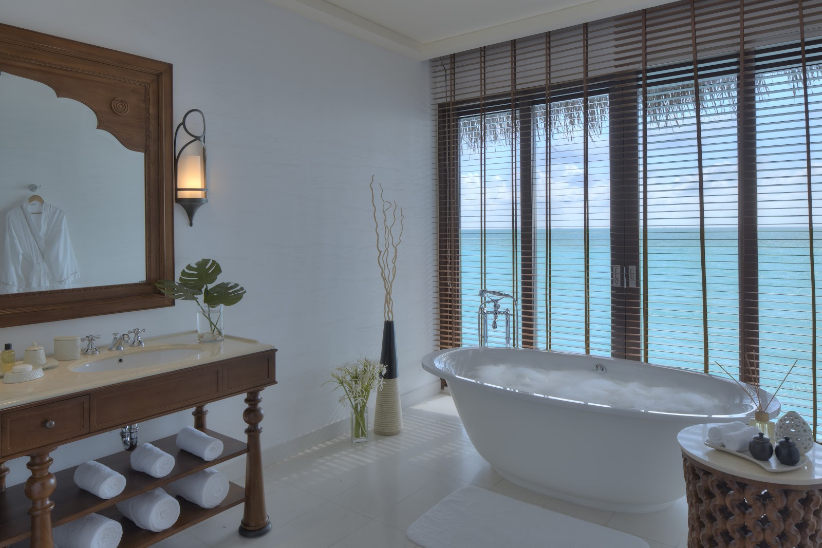 Bathroom with freestanding tub, wood vanity, and ocean views through louvered shutters at The Residence Maldives.