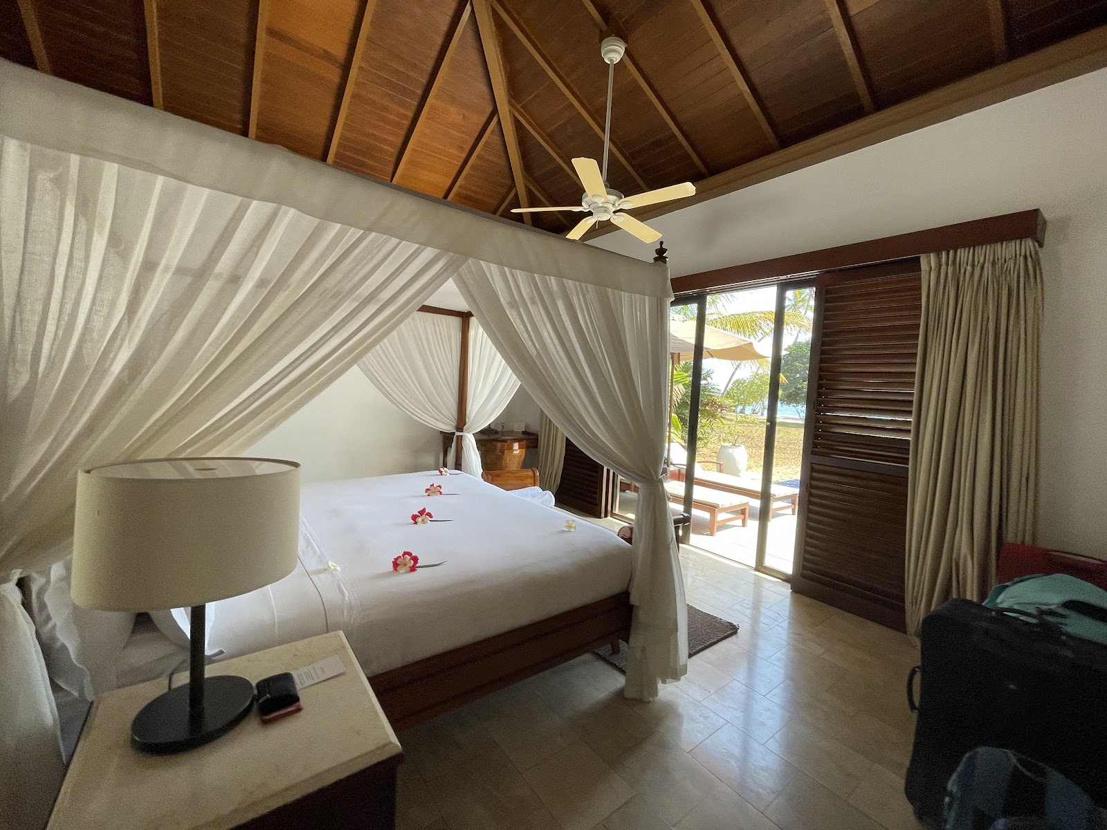 Resort suite with white draped canopy ceiling, wooden bed frame, vanity with mirror, and bedside lamp under peaked tent-like fabric interior.