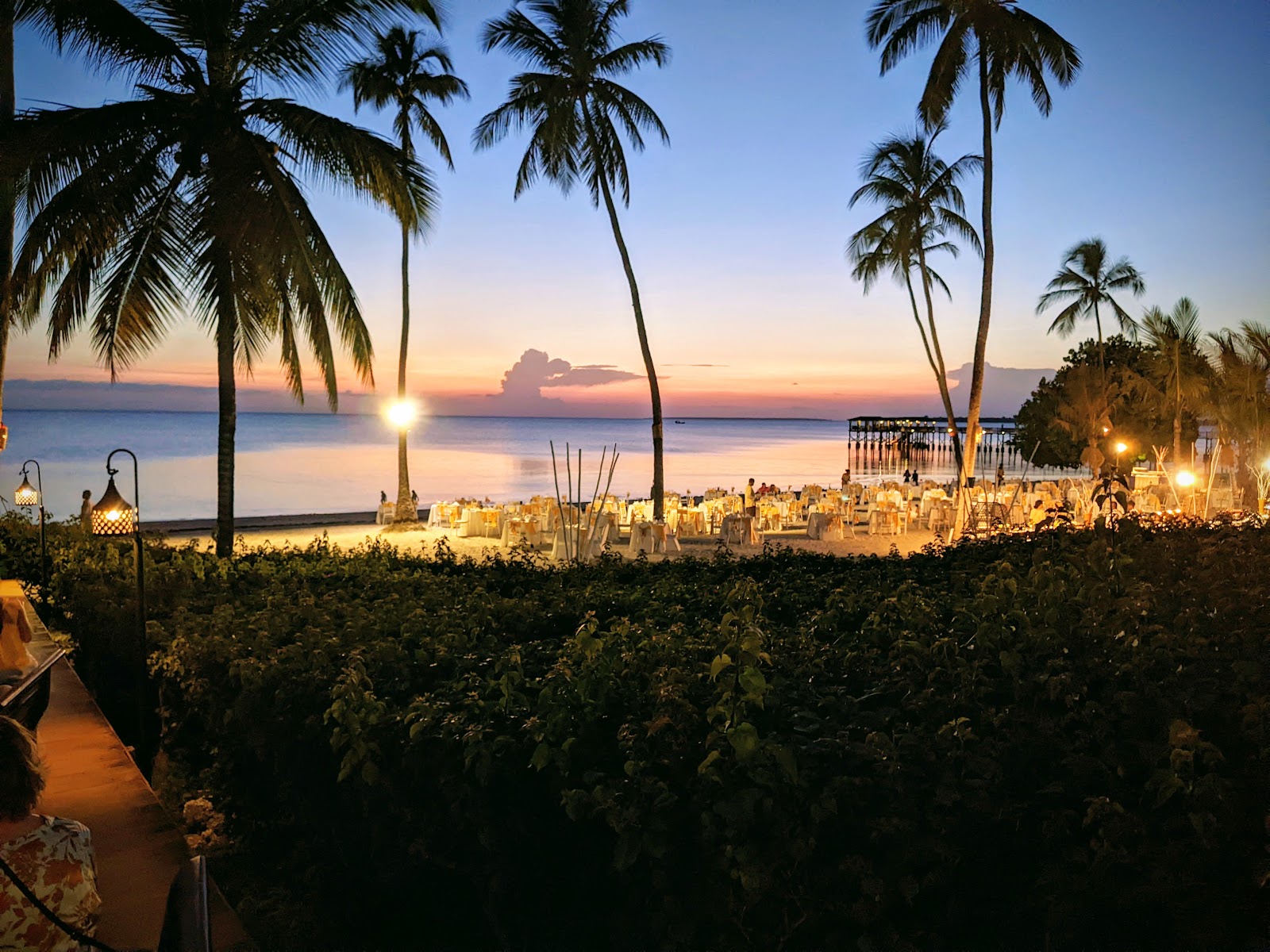 Palm trees frame a beachfront dinner setup at The Residence Zanzibar at sunset, with candlelit tables overlooking calm water.