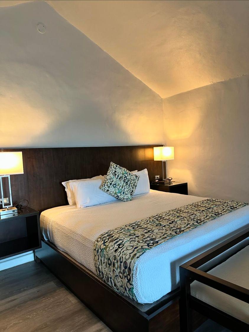 Modern hotel room with a queen bed, patterned bed runner, and bedside lamps illuminating white walls at The Verandah Antigua.