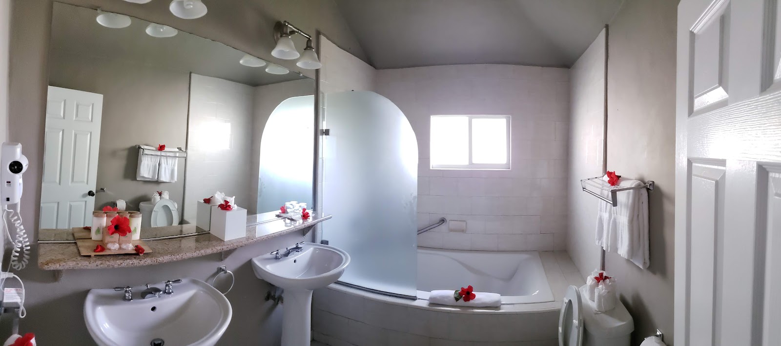 Bathroom with dual sinks, large walk-in shower with glass enclosure, soaking tub, and red flower petals scattered throughout at The Verandah Antigua.