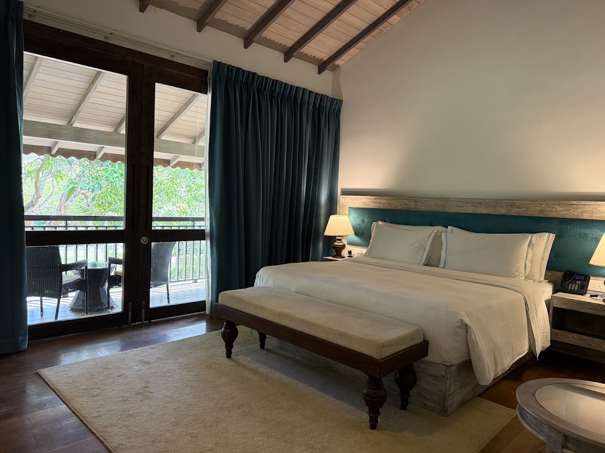 Spacious bedroom with queen bed, green headboard, and dark curtains overlooking a balcony with tree views at The Villas Wadduwa by Amaya.