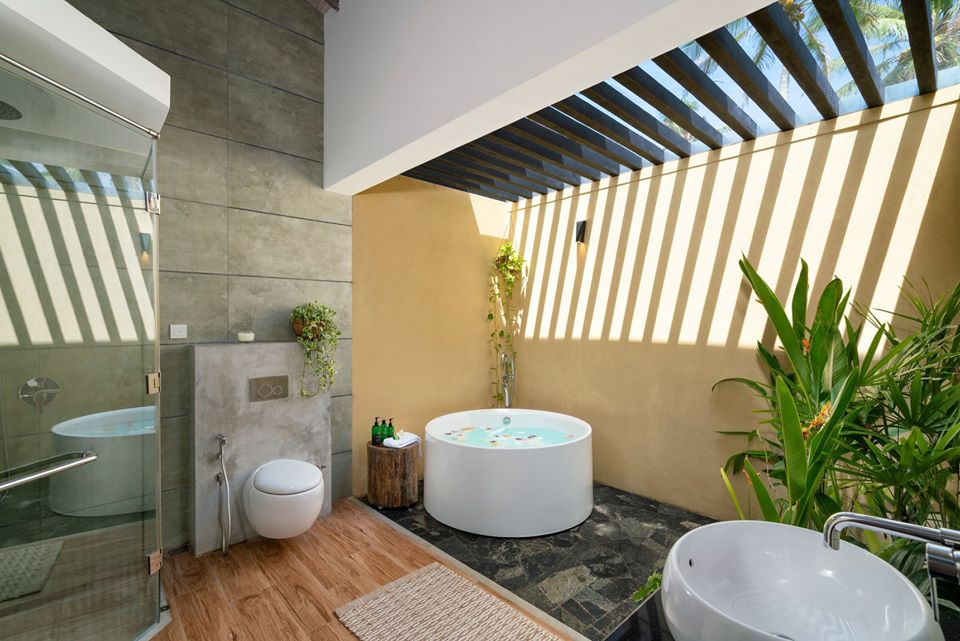 Modern bathroom with yellow walls, round soaking tub, round toilet, and potted plants under a slatted pergola roof.