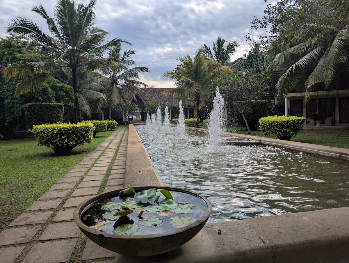 Manicured gardens with palm trees frame a water channel with fountains at The Villas Wadduwa by Amaya, with a lily pond in the foreground.