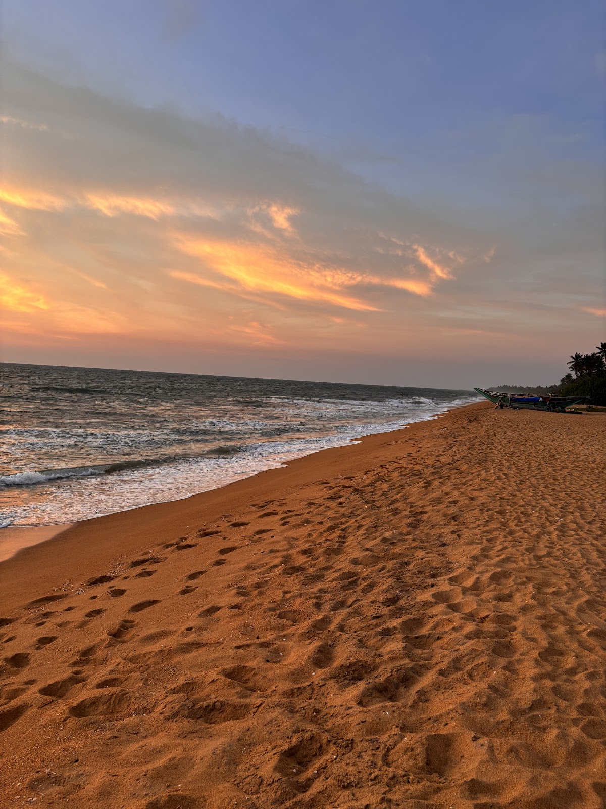 Golden sand beach at sunset with gentle waves and a blue fishing boat anchored offshore at The Villas Wadduwa by Amaya.