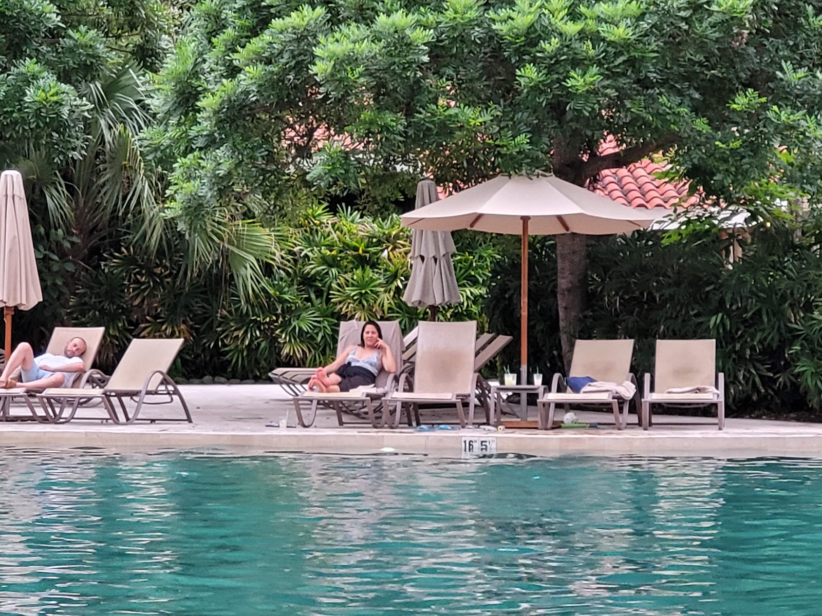 Guests relax on lounge chairs beside a pool at The Westin Reserva Conchal, with umbrellas and lush vegetation in the background.