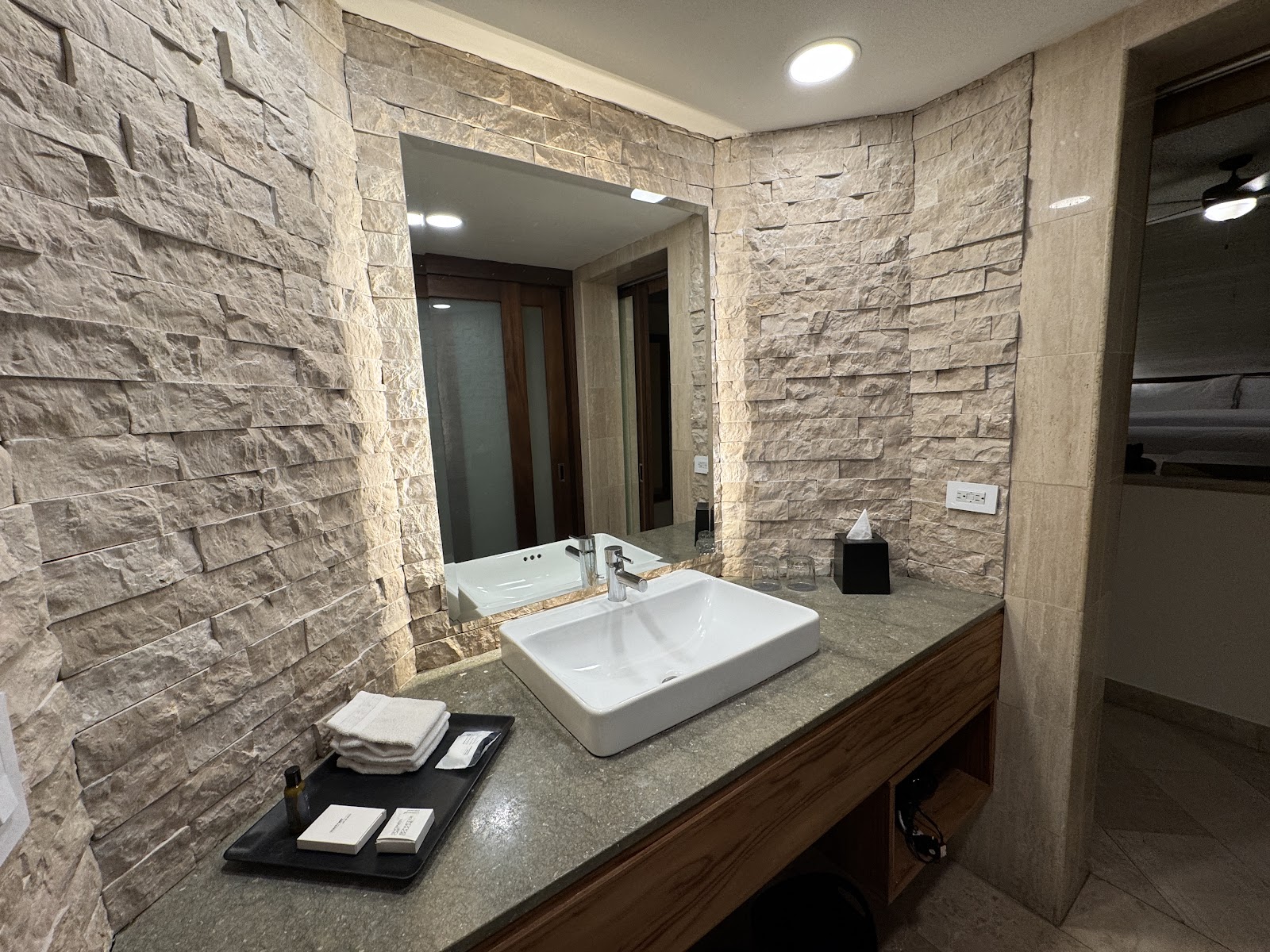 Modern bathroom with textured stone walls, white rectangular sink, and granite countertop at The Westin Reserva Conchal.