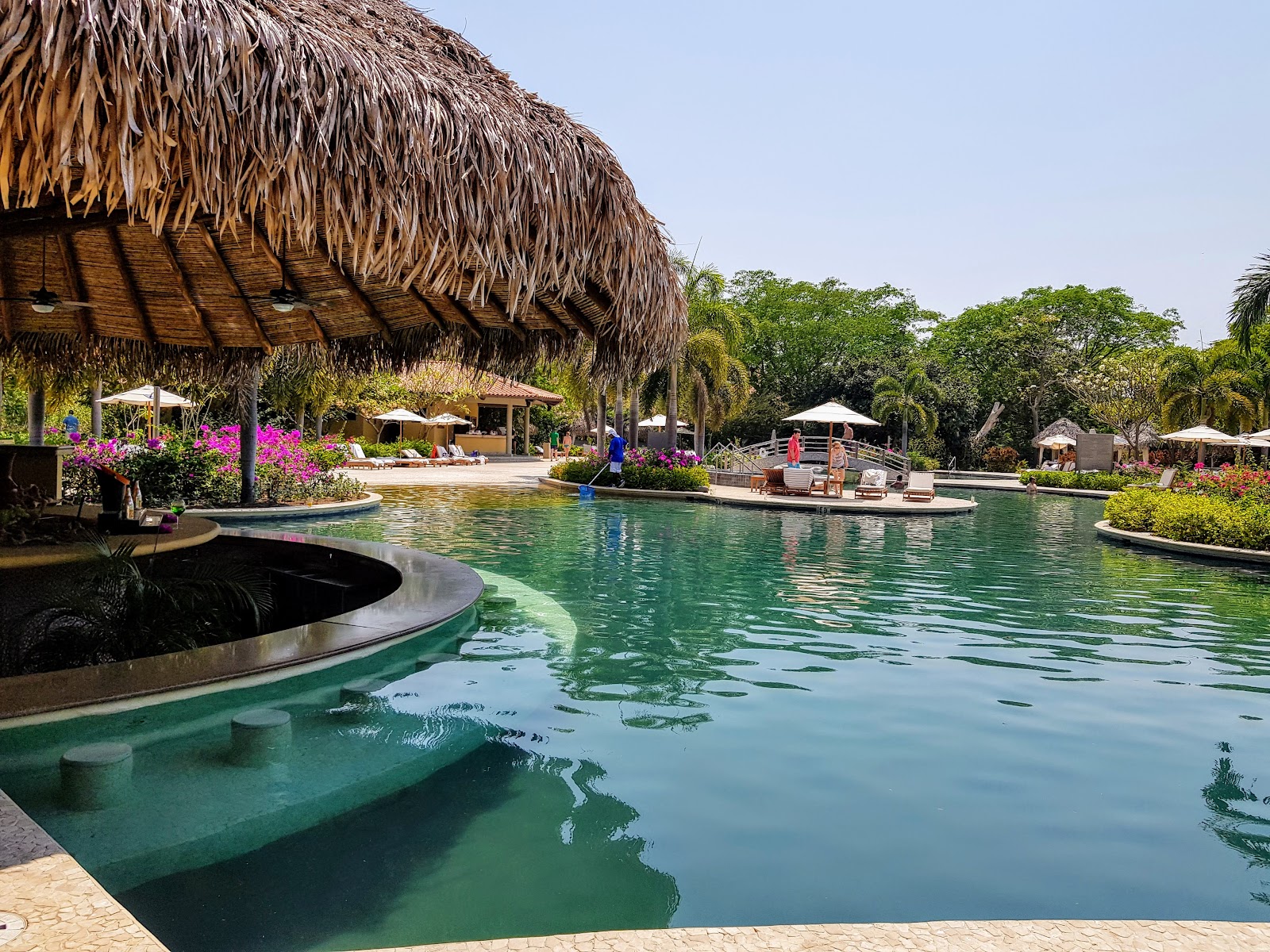 Turquoise pool with sunken seating areas, large thatched-roof palapa, magenta bougainvillea, and tropical landscaping at The Westin Reserva Conchal.