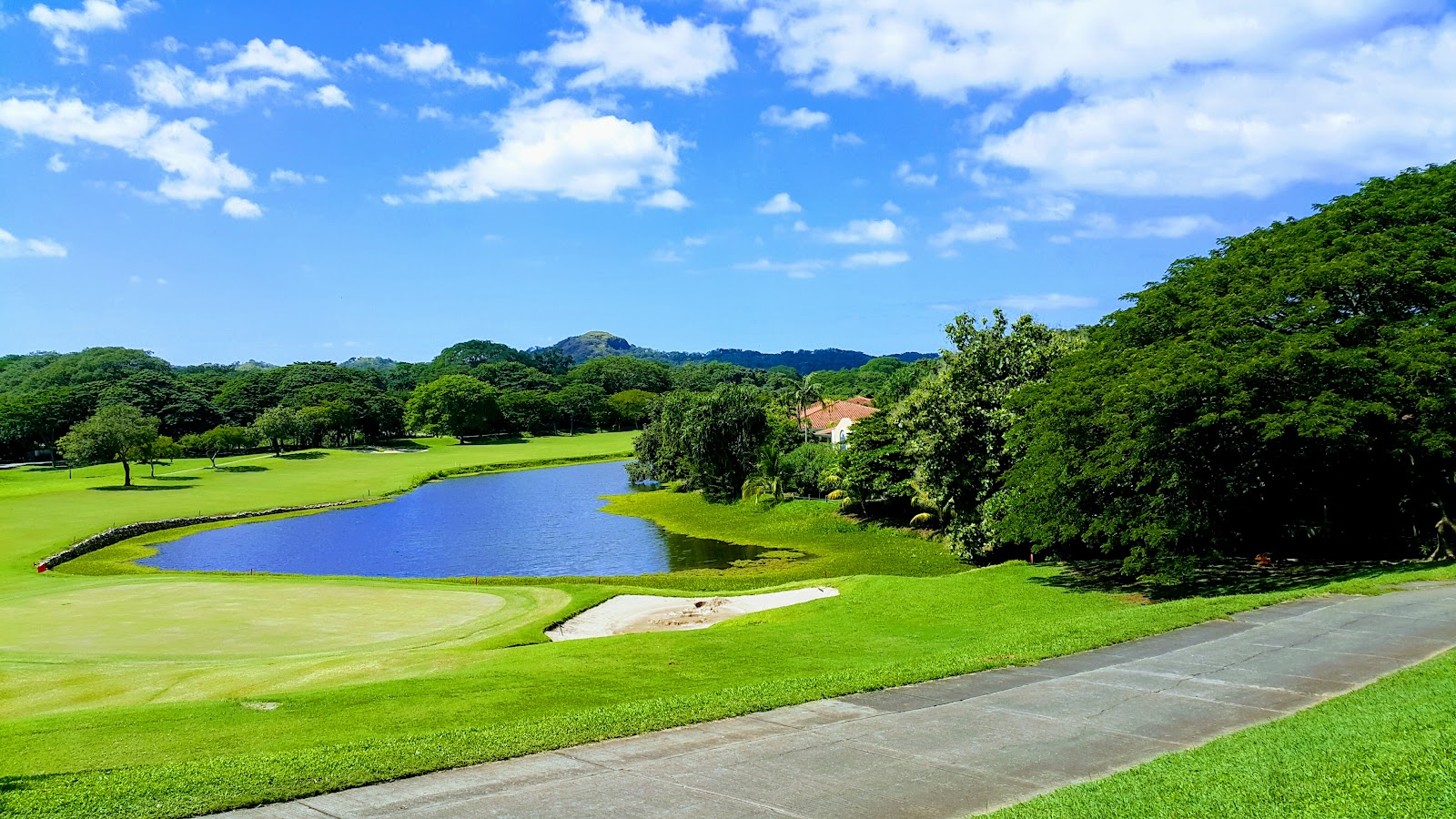 Golf course with a blue lagoon, sand bunker, manicured fairways, and forested hills under a partly cloudy sky at The Westin Reserva Conchal.