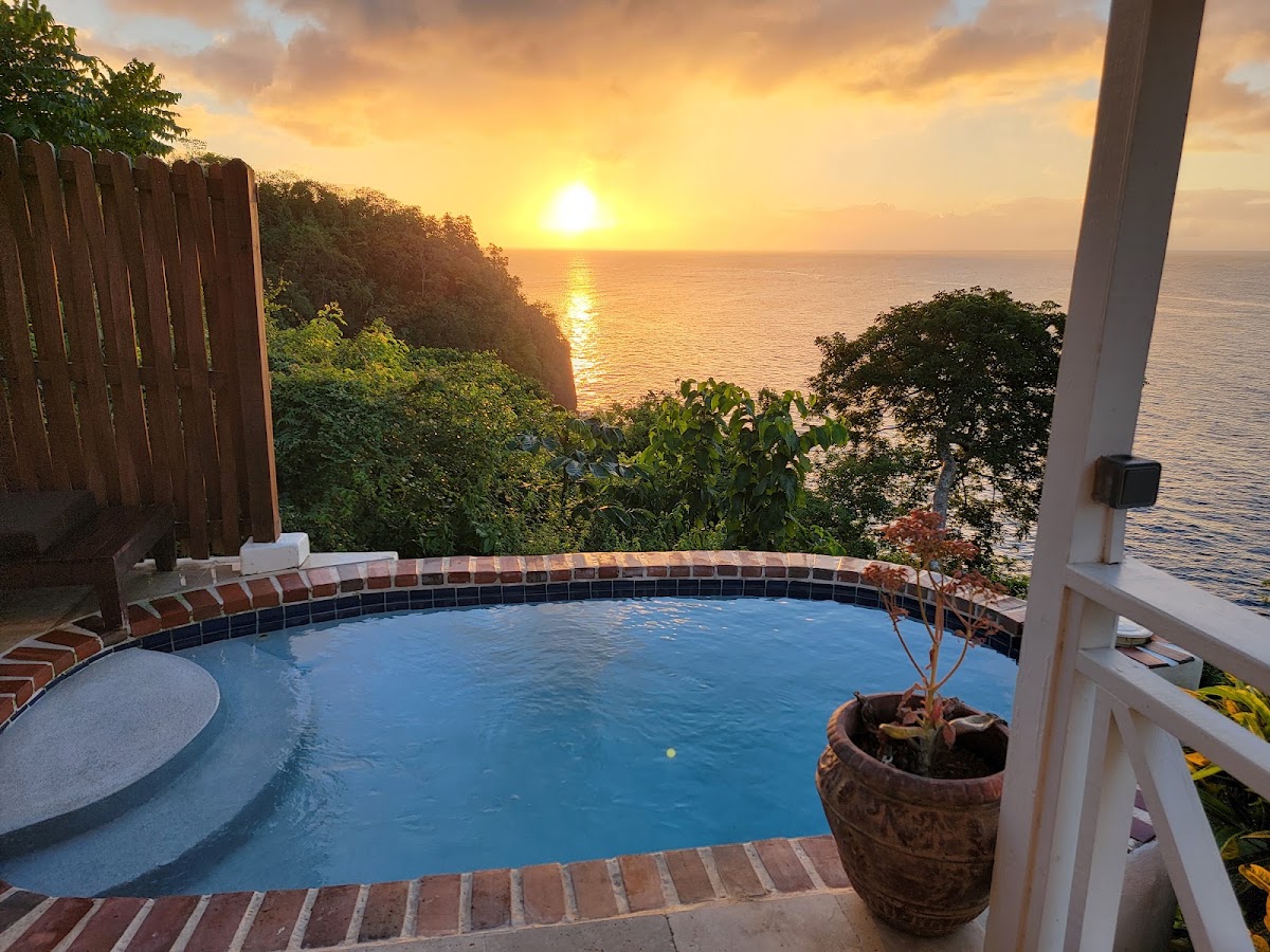 Clifftop pool at Ti Kaye Resort & Spa overlooks the Caribbean Sea at sunset, with tropical vegetation and wooden railings framing the view.