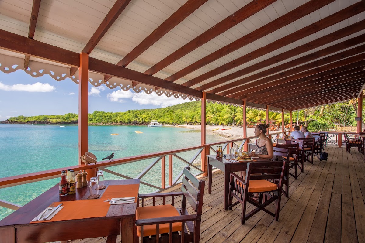 Beachfront dining pavilion at Ti Kaye Resort & Spa with turquoise water, wooden deck, and tropical coastline beyond.