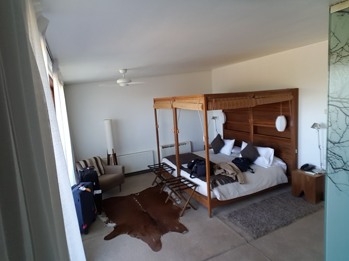 Spacious resort bedroom with wooden four-poster bed, seating area, and animal hide rug on concrete floor at Tierra Atacama.