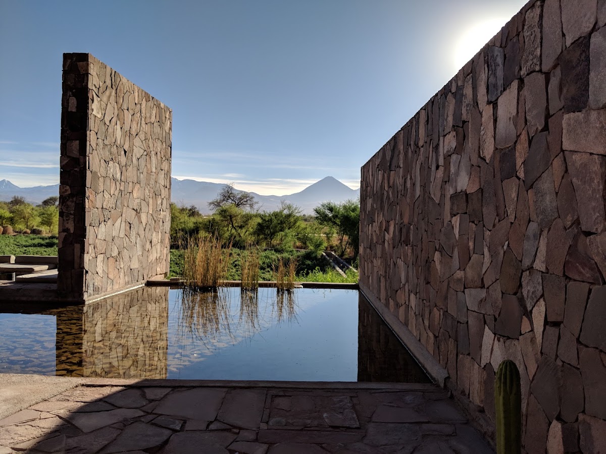 Stone walls frame a reflecting pool with volcano views and green landscape beyond at Tierra Atacama.