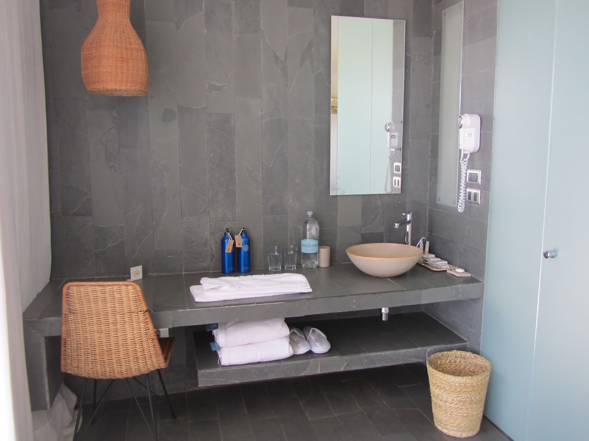 Bathroom vanity with gray tile walls, round beige sink, mirror, woven pendant lamp, and wicker chair at Tierra Atacama.