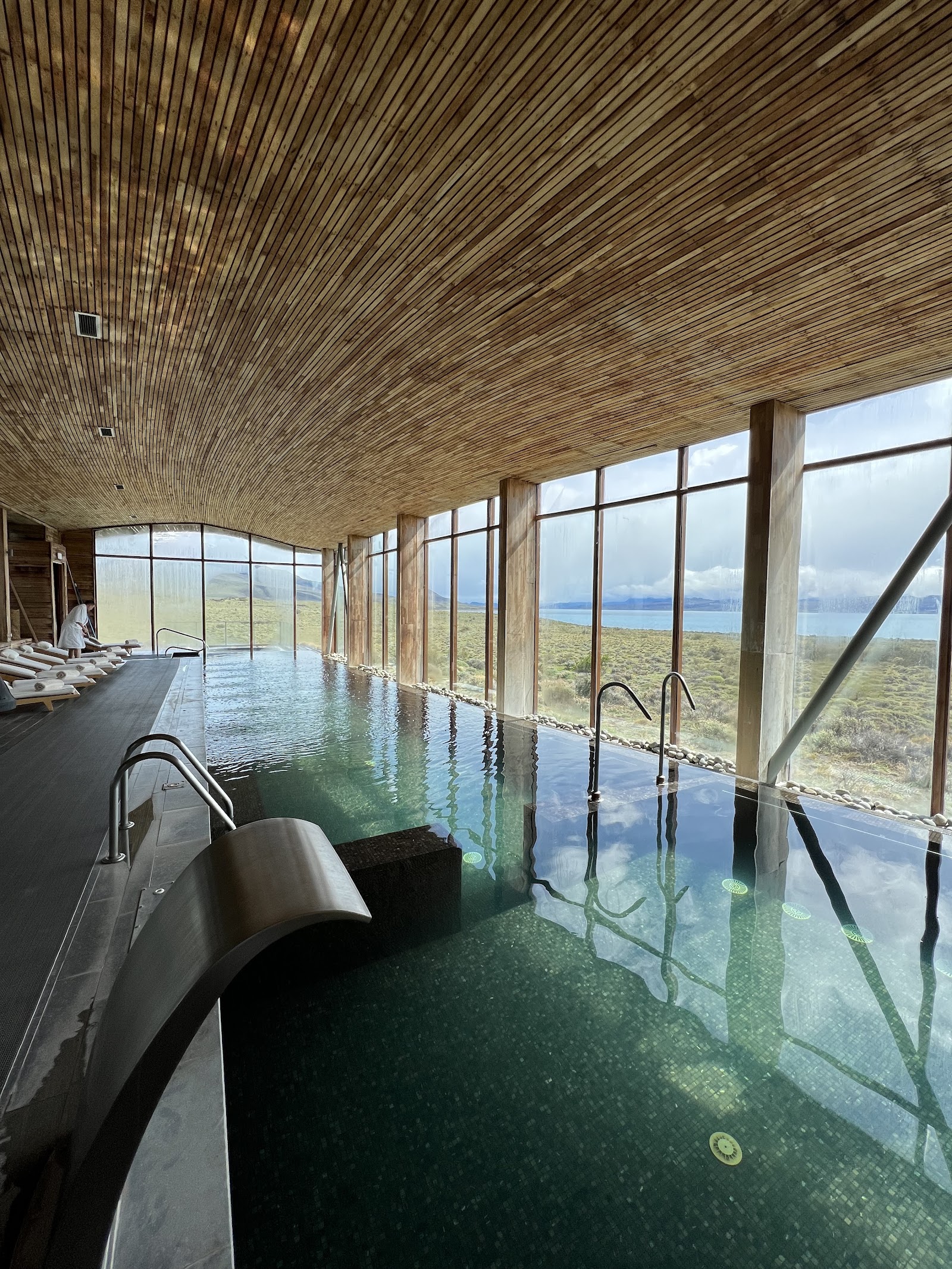 Indoor geothermal pool with floor-to-ceiling windows overlooking Patagonian steppe and distant lake at Tierra Patagonia.