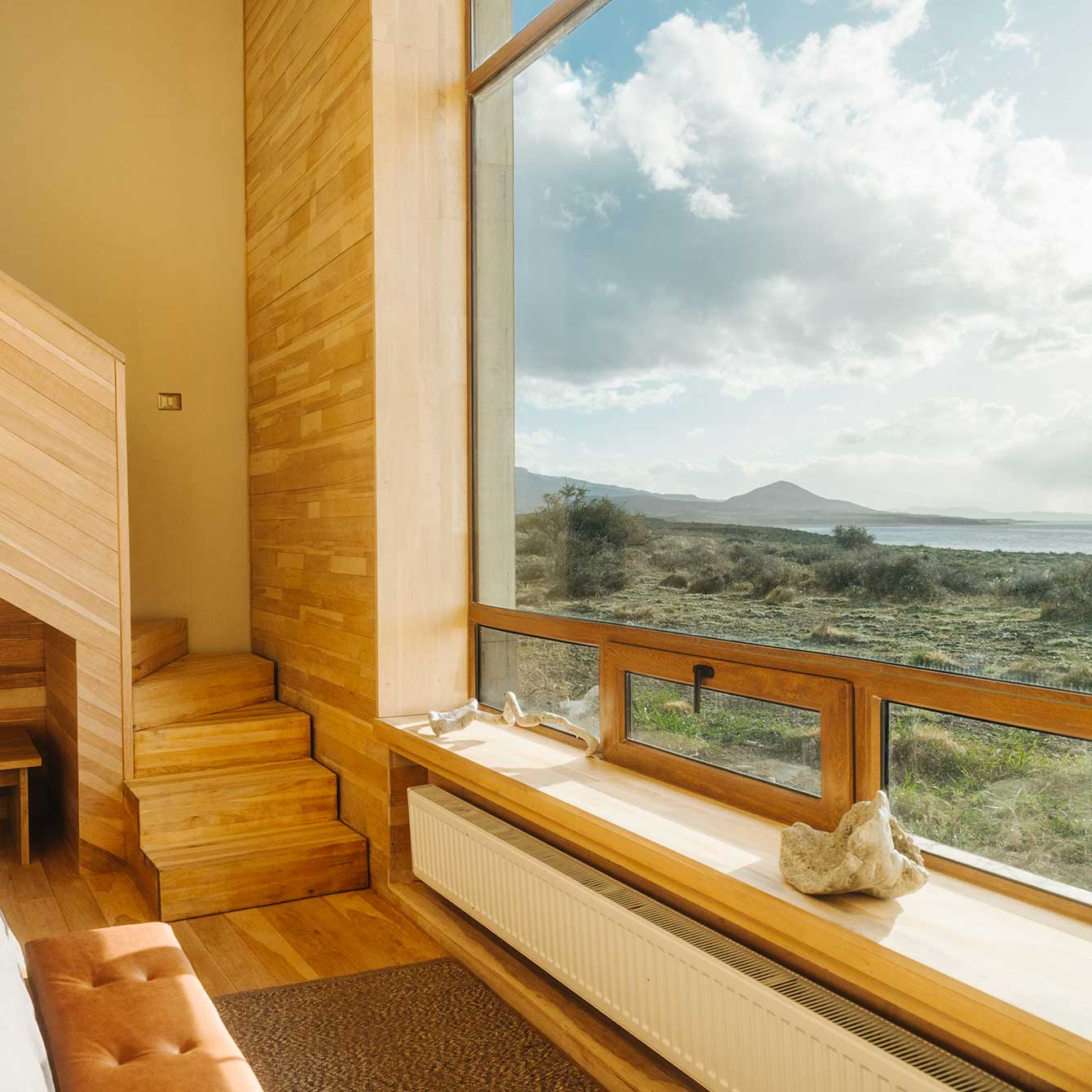 Wood-paneled resort suite with bed, sofa, and round soaking tub, large window framing snow-capped mountains and twilight lake views.