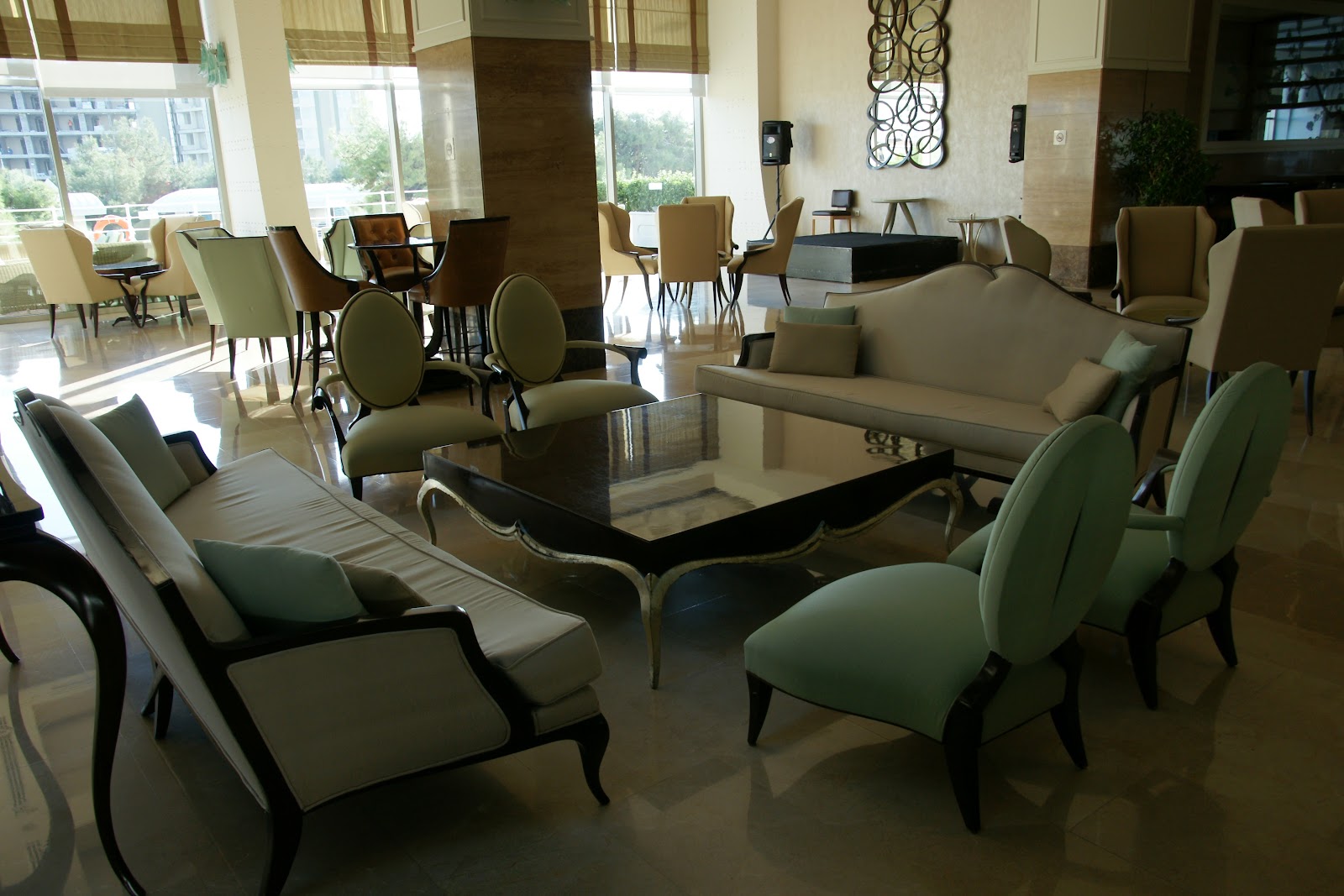 Spacious lobby lounge at Titanic Deluxe Lara with cream and green upholstered seating, black coffee table, and large windows overlooking the grounds.