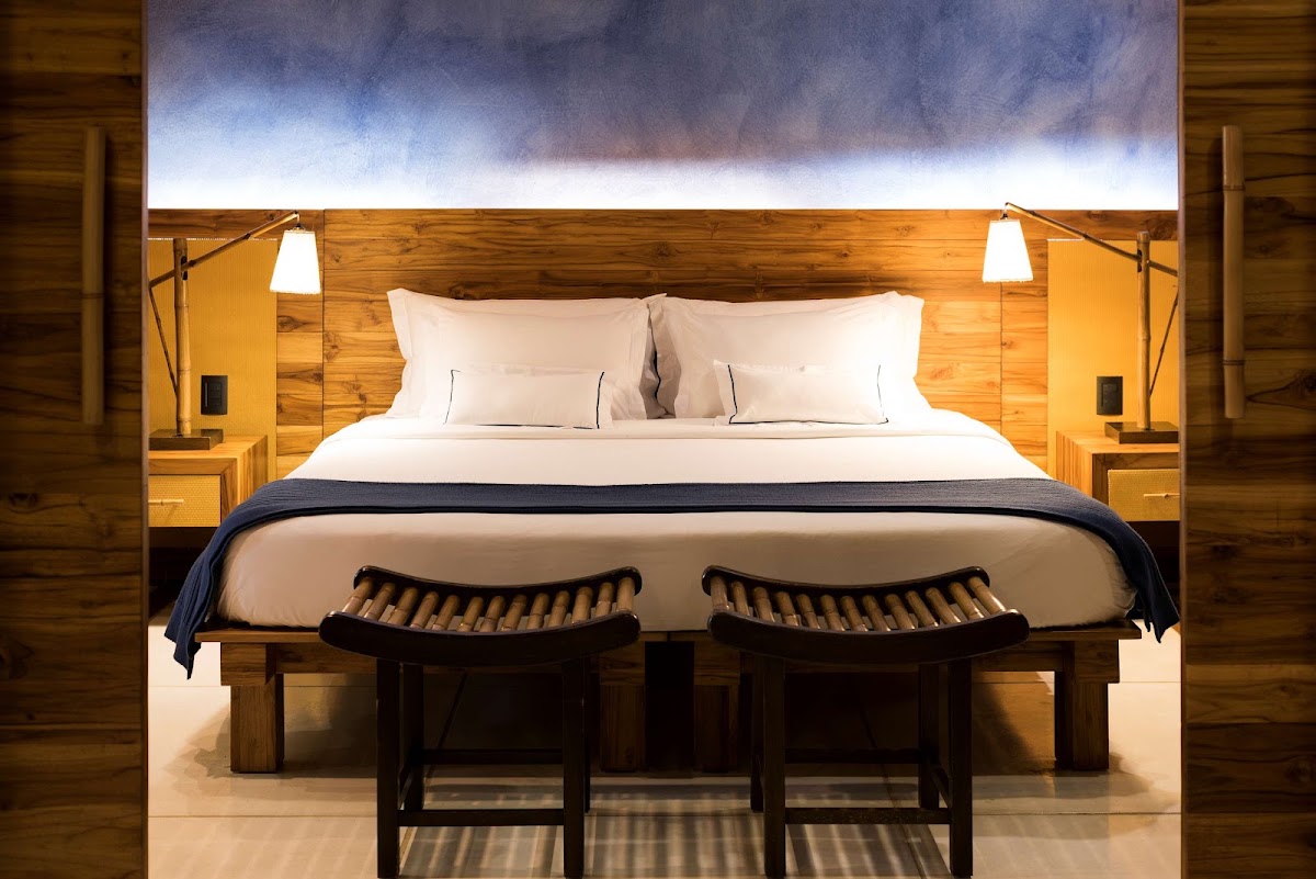 Wooden bedroom with king bed, white linens, two dark wood benches at foot, and illuminated headboard backdrop.