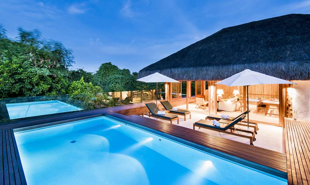 Two illuminated pools with wooden decking, lounge chairs under white umbrellas, and thatched-roof bungalows at Tivoli Ecoresort Praia do Forte surrounded by tropical vegetation.