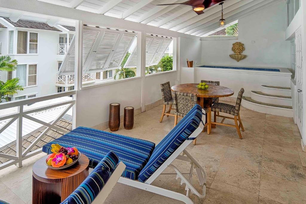 Covered patio at Treasure Beach Art Hotel with blue striped loungers, wooden dining table, and white colonial-style building visible through louvered windows.