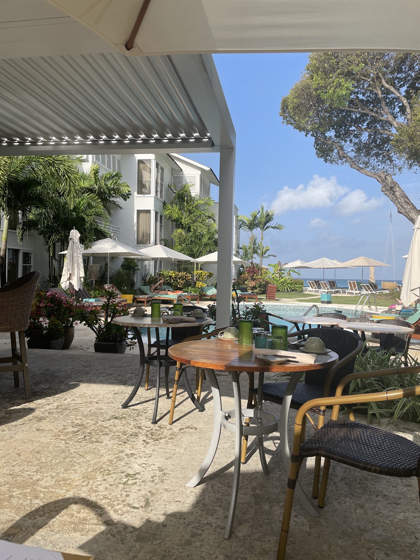 Shaded patio with dining tables overlooking the pool, beach, and ocean at Treasure Beach Art Hotel.