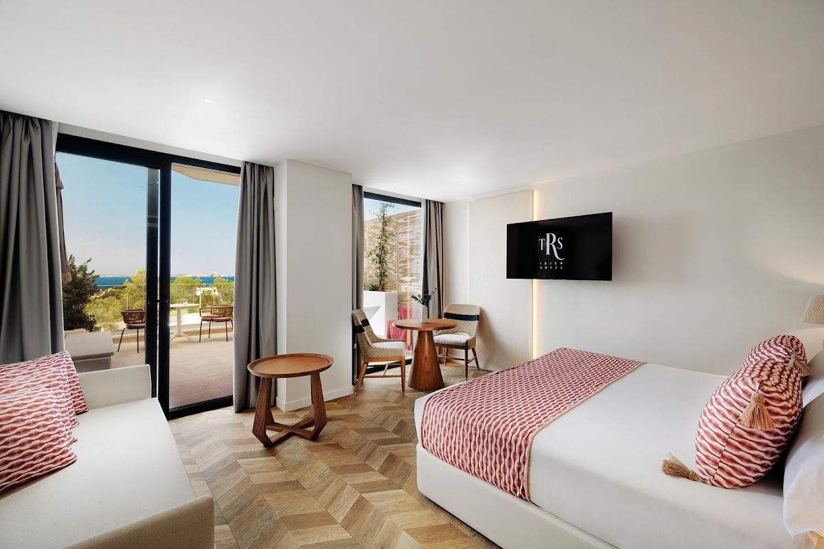 Resort bedroom at TRS Ibiza with two beds, sea views from balcony, and modern furnishings in white and coral tones.