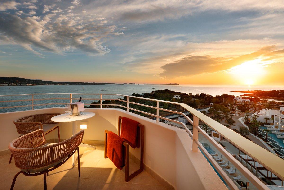 Sunset view from a terrace at TRS Ibiza with woven chairs, sea beyond, and coastal hills on the horizon.