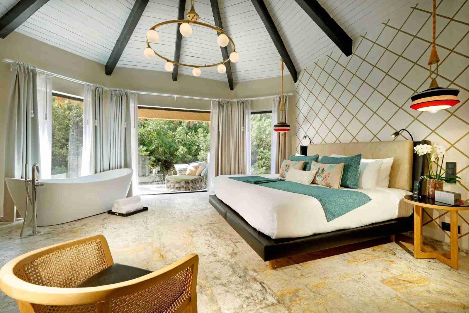 Spacious resort suite with soaking tub, king bed with green bedding, round skylight, and floor-to-ceiling windows overlooking gardens.