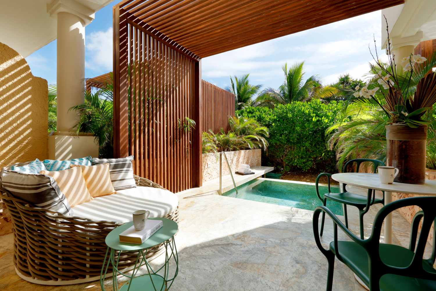 Private patio with lounge chairs, wooden pergola, small plunge pool, and dining table surrounded by tropical plants and palm trees.