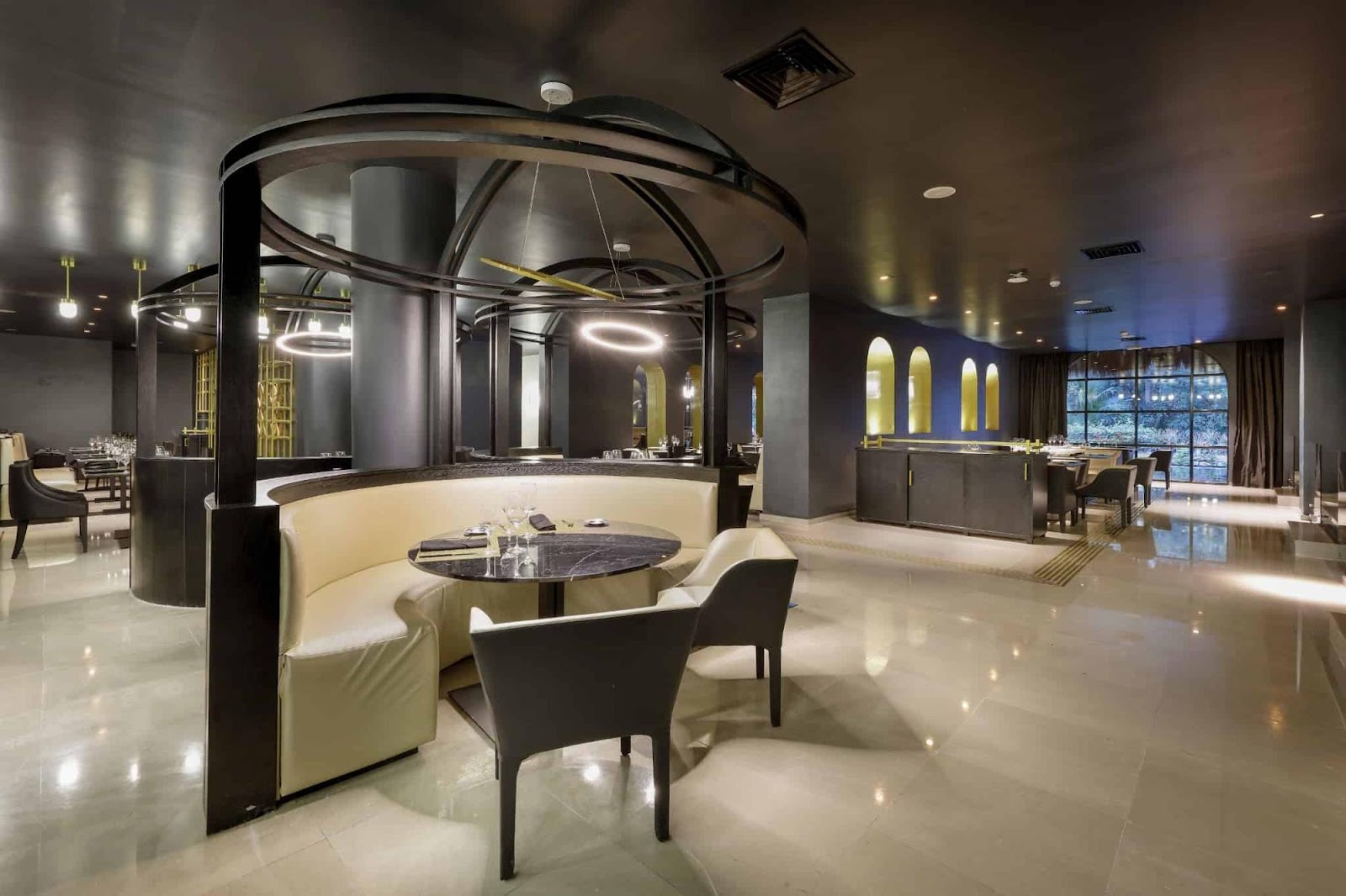 La Boheme bar at TRS Yucatan Hotel features a curved counter with white bar stools, illuminated ceiling, and shelves of liquor bottles.