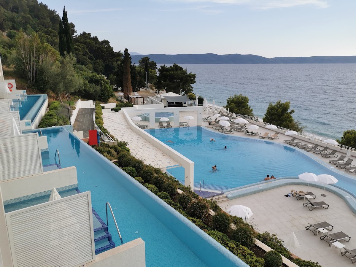 TUI BLUE Adriatic Beach's cascading pools overlook the Adriatic Sea, with loungers, cypress trees, and distant mountains under clear sky.
