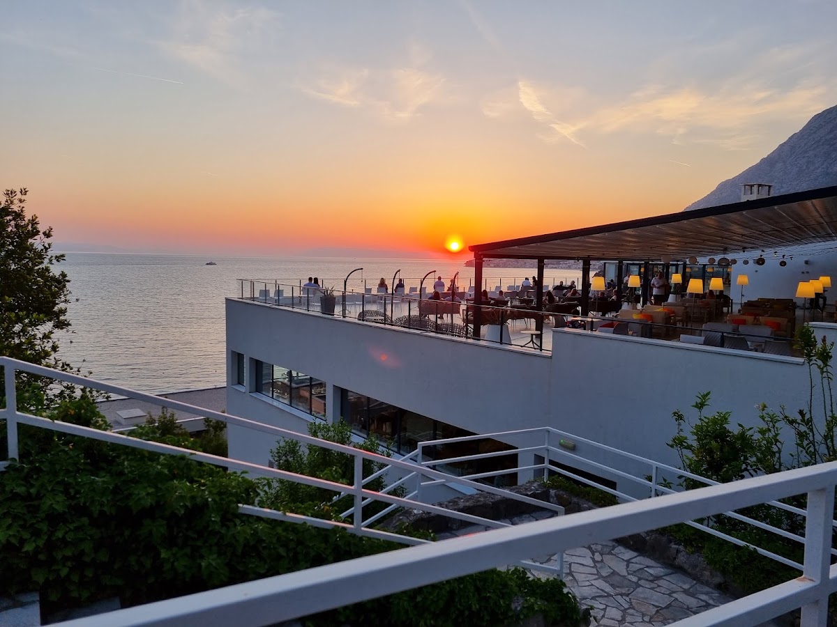 Sunset at TUI BLUE Adriatic Beach with diners on a waterfront terrace overlooking the Adriatic Sea and mountains beyond.
