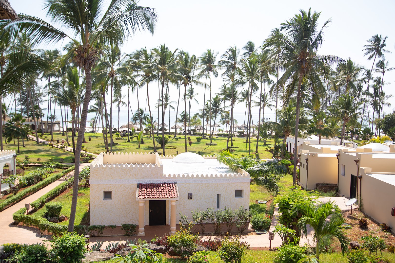 White villa with crenellated roof among palm trees and manicured grounds at TUI BLUE Bahari Zanzibar, with ocean visible in distance.