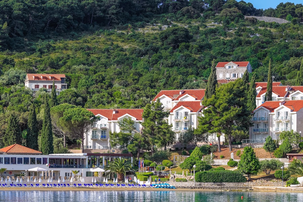 TUI BLUE Kalamota Island beachfront with white villas featuring red-tiled roofs nestled among cypress trees on a forested hillside.