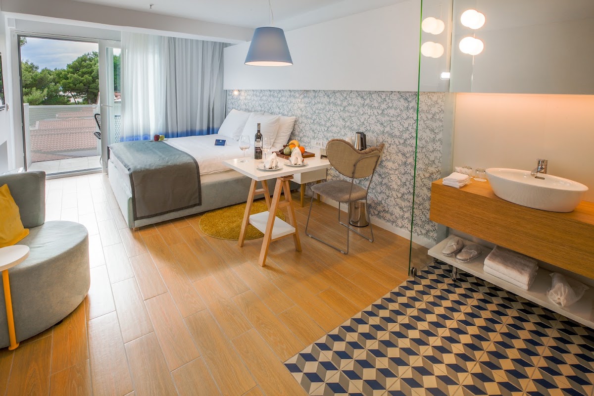 Modern resort room with queen bed, work desk, freestanding bathtub, and balcony overlooking trees at TUI BLUE Makarska.