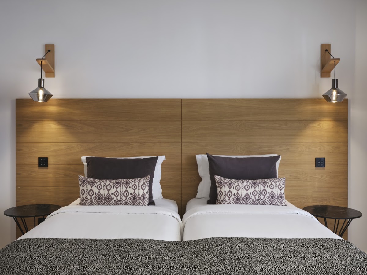 Two double beds with wooden headboard, black and white patterned pillows, and brass wall sconces in a modern resort bedroom.