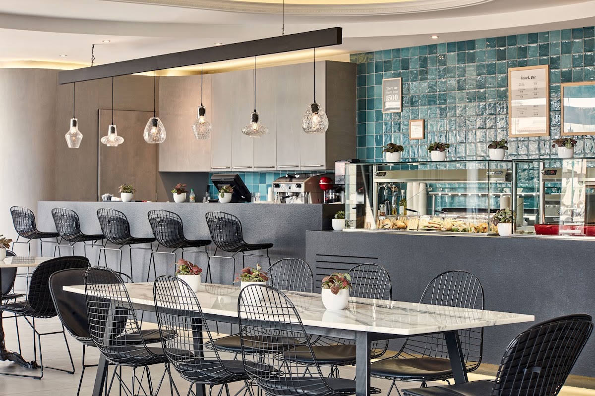 Modern snack bar with turquoise tile backsplash, marble-topped dining table, black wire chairs, and pendant lighting overhead.